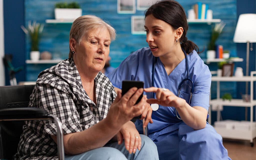 Nurse assisting elderly patient with using cell phone